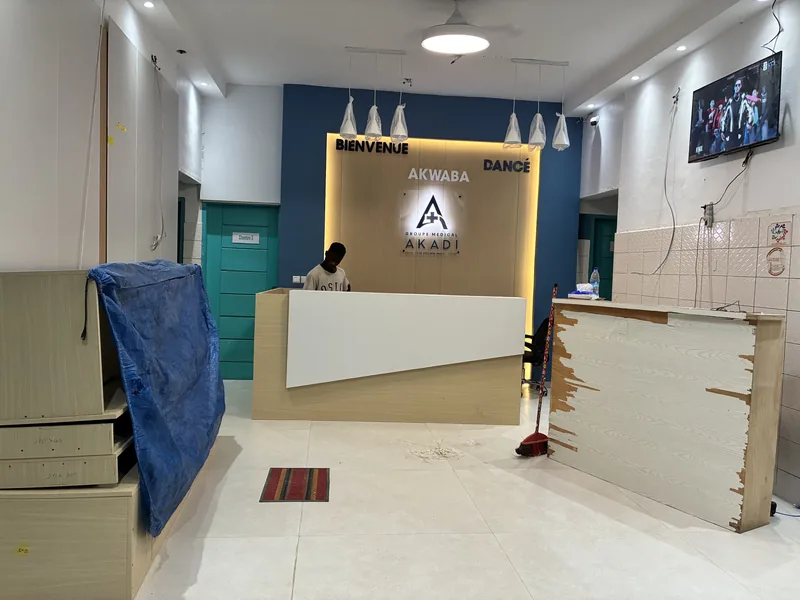 Groupe Médical AKADI, pendant — La banque posée et le mur d'identité allumé, luminaires encore sous emballage.
